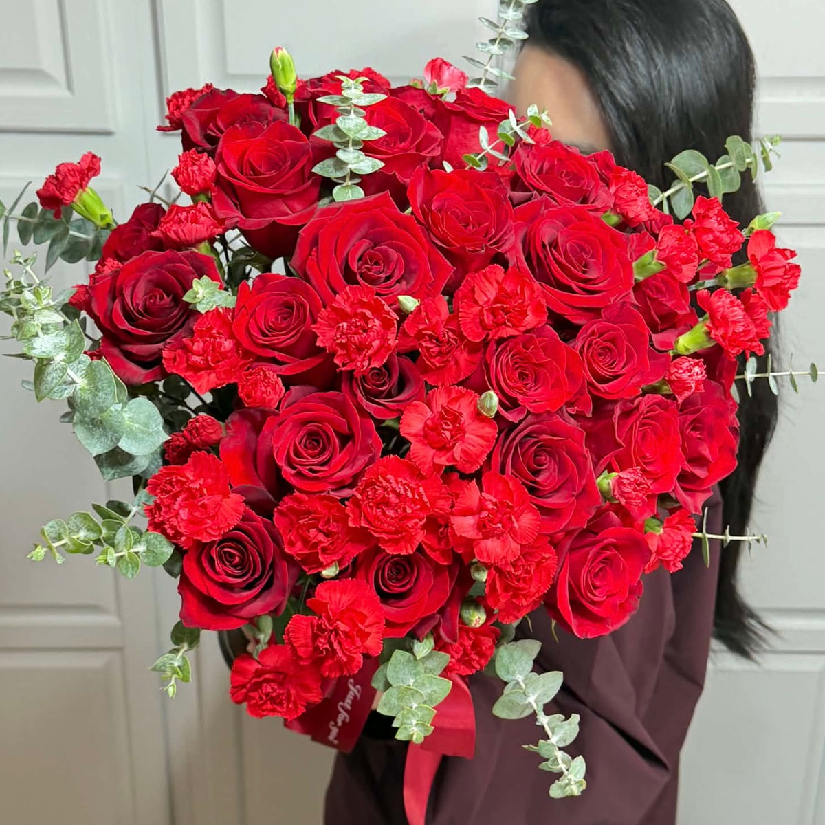 Vibrant red roses and carnations bouquet with green eucalyptus leaves.