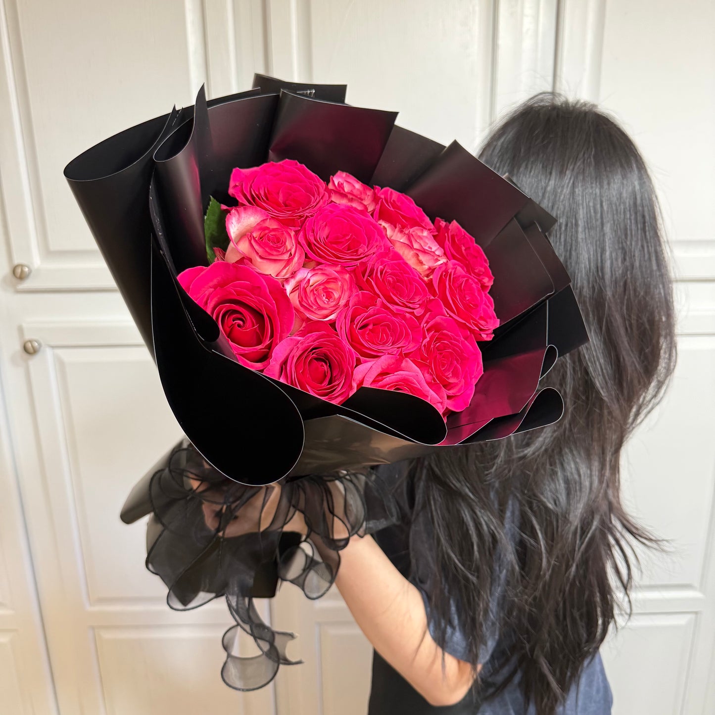 Vibrant pink roses in a large bouquet wrapped in elegant black paper and ribbon.