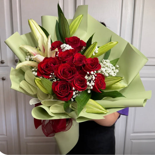 A vibrant bouquet of red roses and white lilies wrapped in light green paper.