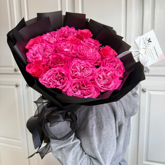 Vibrant pink roses in a large black paper bouquet with ribbon.