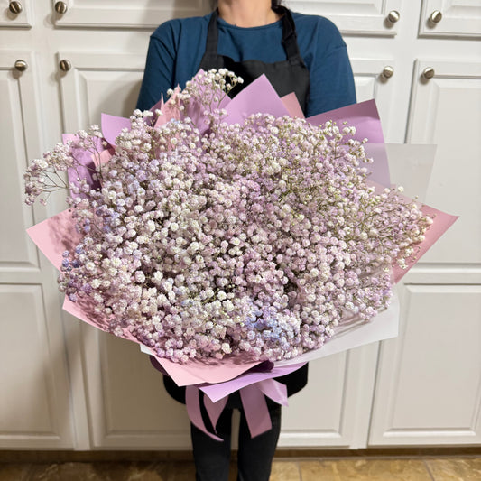 Large bouquet of delicate pink, purple, and white baby's breath flowers wrapped in paper.