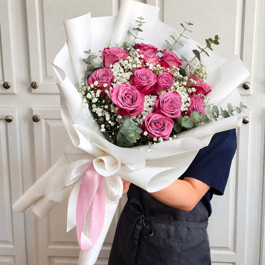 Vibrant pink rose bouquet with baby's breath and eucalyptus, wrapped in white with a pink ribbon.