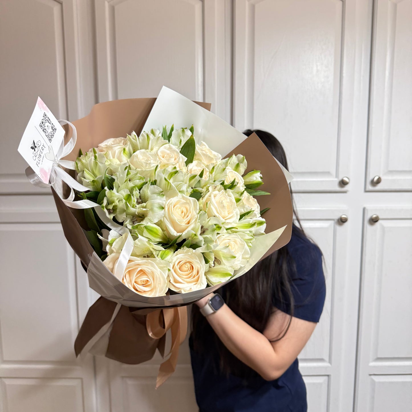 Large bouquet of cream roses and green filler flowers in brown and white wrap.