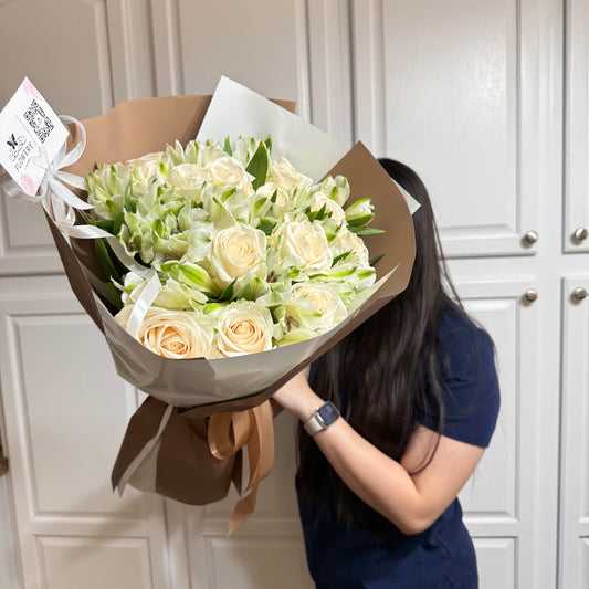 Cream roses and green flowers in a large brown-wrapped bouquet held by a person.