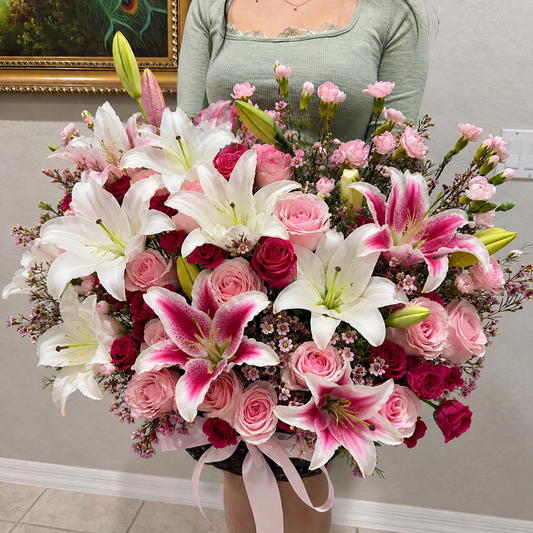 A large, vibrant bouquet of white and pink lilies and roses with a pink ribbon.