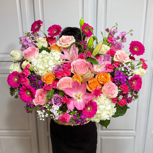 A large, vibrant floral arrangement with pink, orange, and white flowers in a basket.