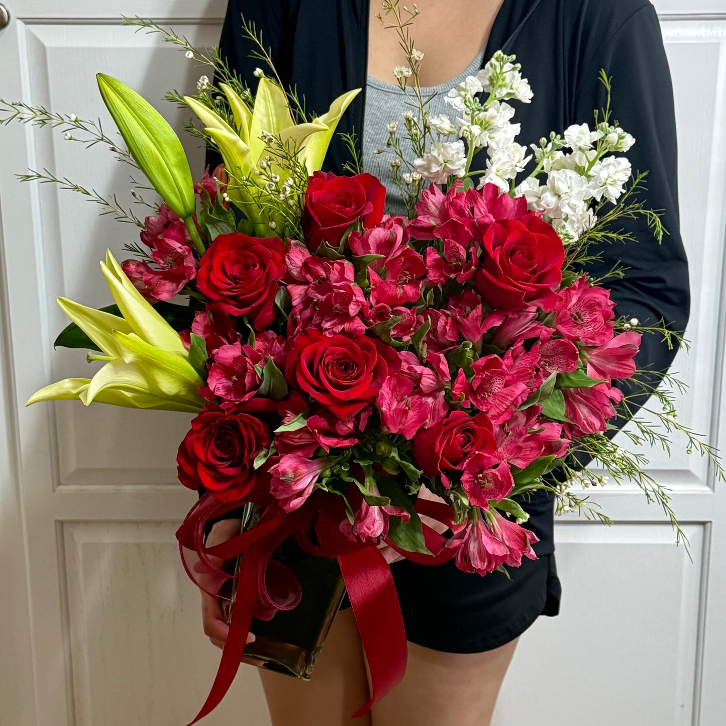 A lovely bouquet featuring red roses, yellow lilies, and white flowers.