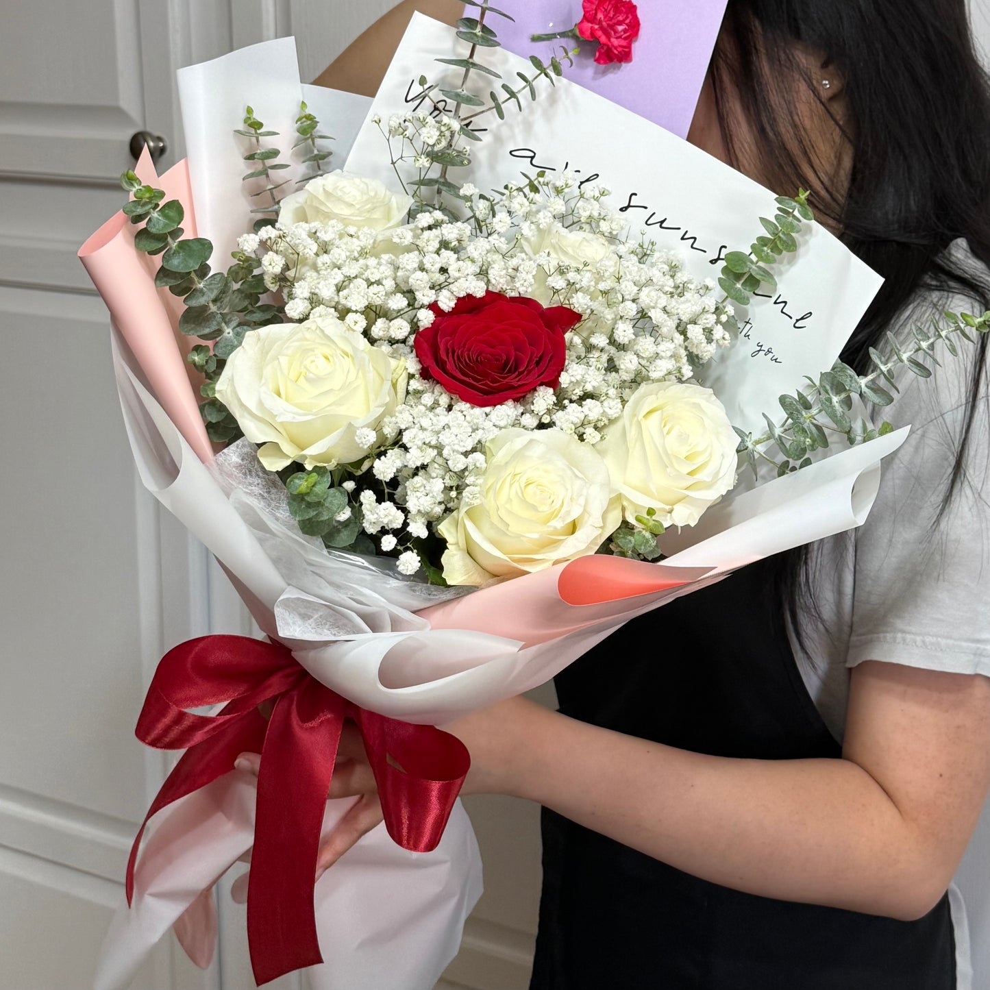 Bouquet of white and red roses, baby's breath, wrapped in pink paper.