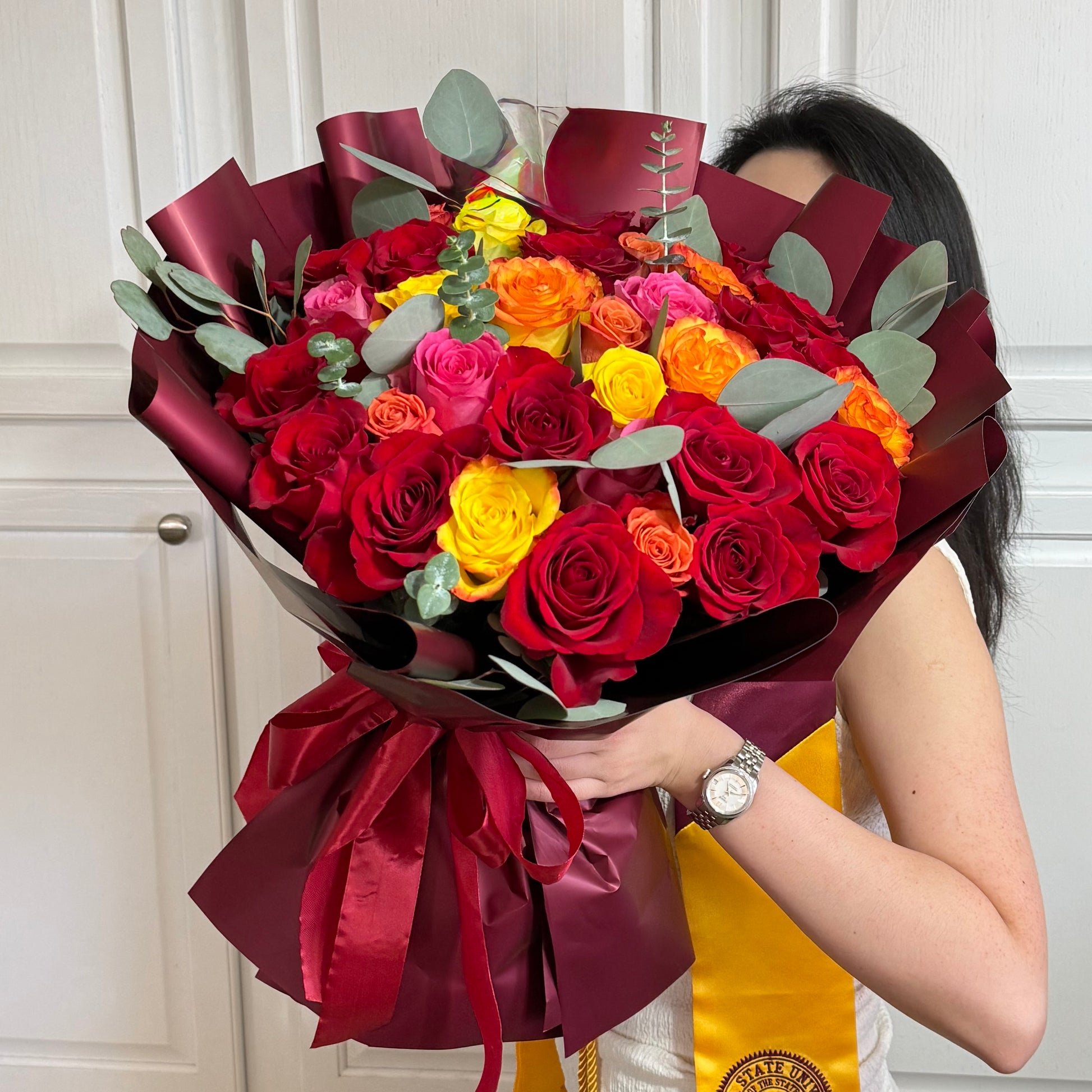 A vibrant bouquet of red, yellow, orange, and pink roses with eucalyptus leaves.