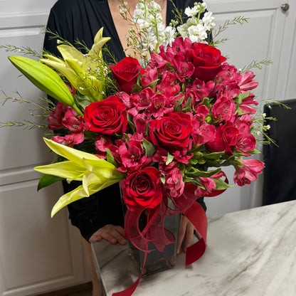 A lovely bouquet of red roses, yellow lilies, and white flowers in a clear vase.