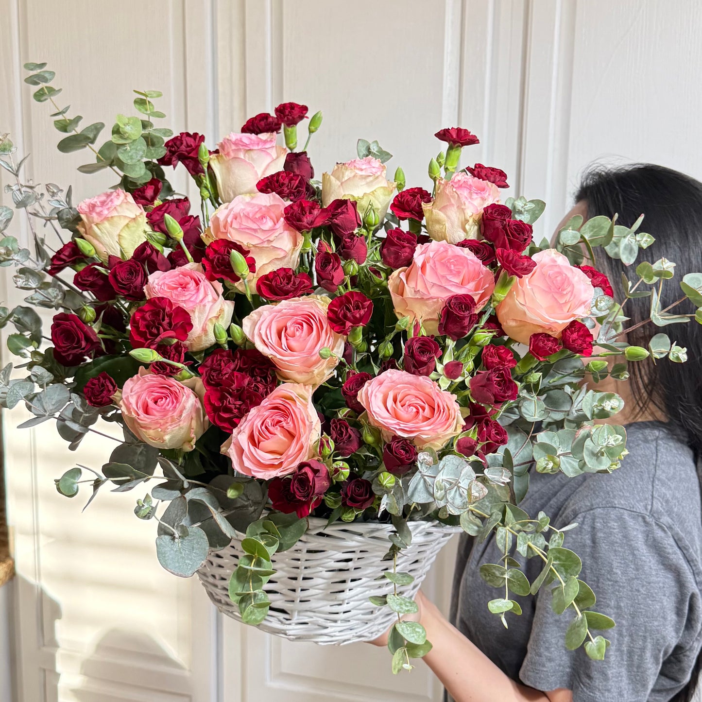 Vibrant pink and deep red roses and carnations in a white woven basket.