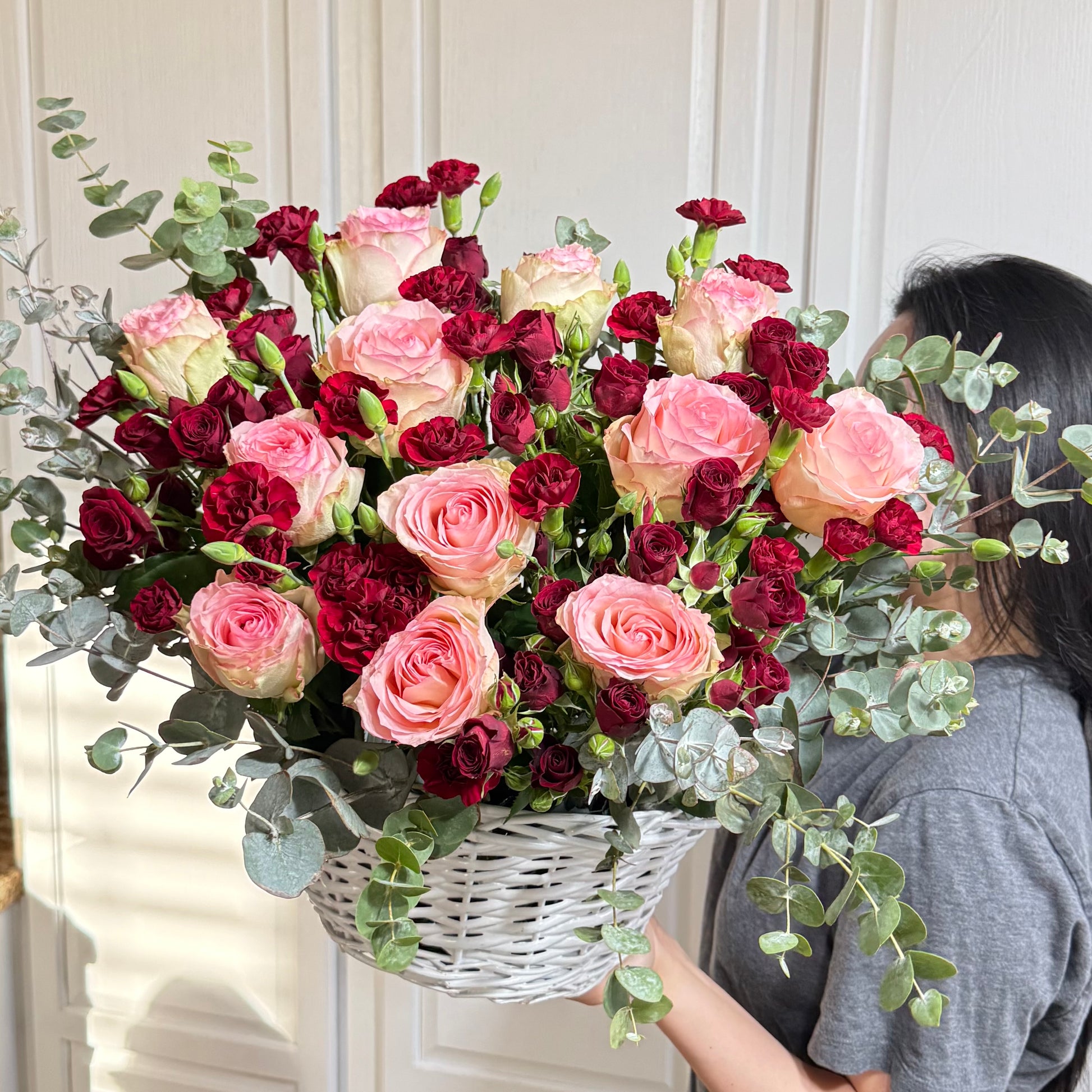 Vibrant pink and deep red roses and carnations in a white woven basket.