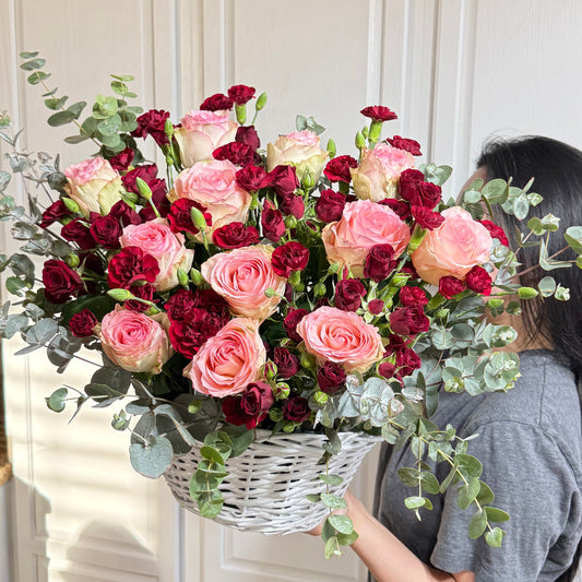 Vibrant pink and deep red roses and carnations in a white woven basket.