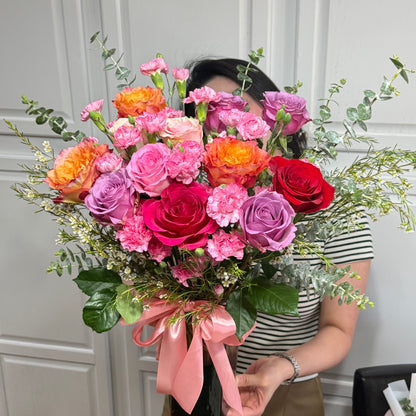 Vibrant bouquet of pink, orange, red, and purple roses and carnations.