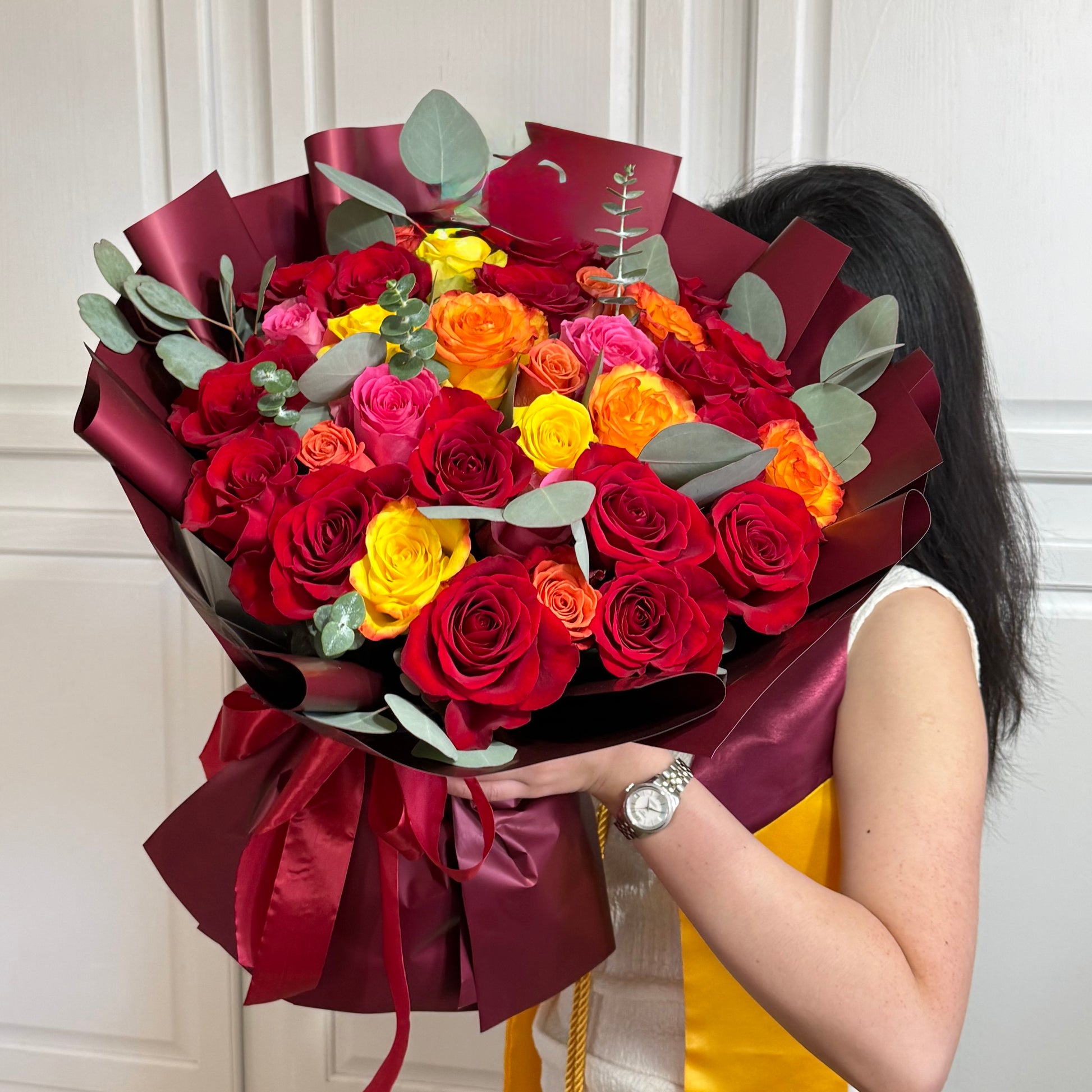 Vibrant sunset-colored rose bouquet with red, yellow, and orange flowers, wrapped in burgundy.