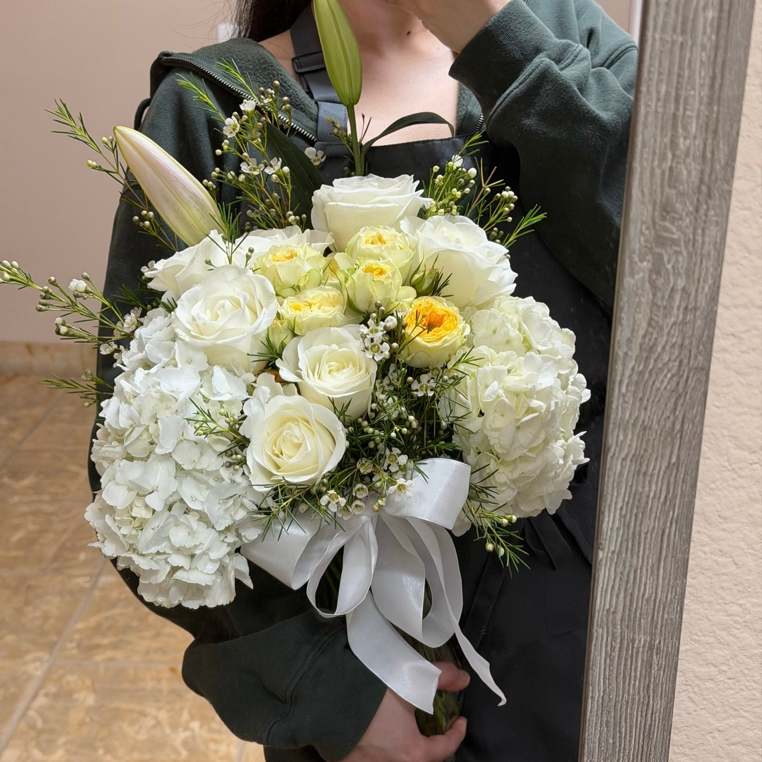 Large white and yellow floral bouquet with roses, hydrangeas, and a white ribbon.