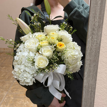 Large white and yellow floral bouquet with roses, hydrangeas, and a white ribbon.