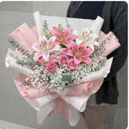 Pink and white lily and rose bouquet with baby's breath, wrapped in paper.