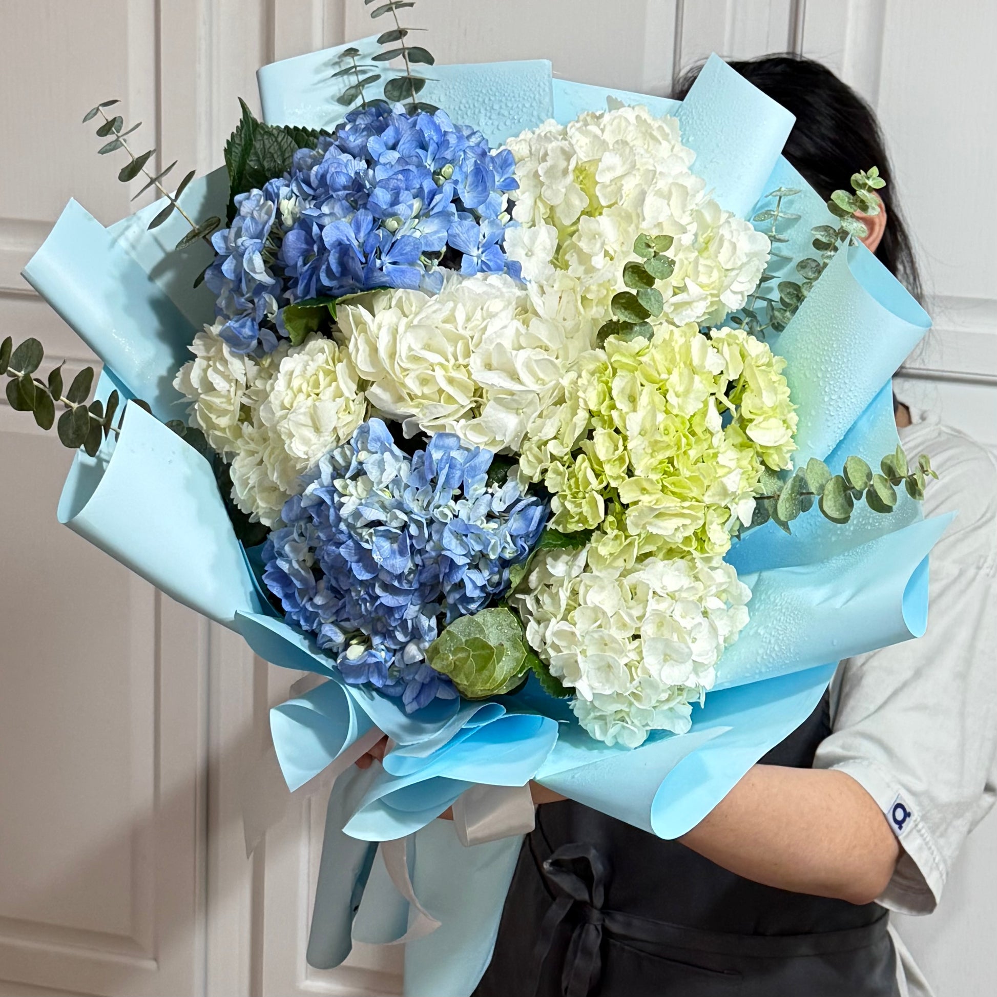 Fresh blue, white, and green hydrangea bouquet in light blue wrapping.