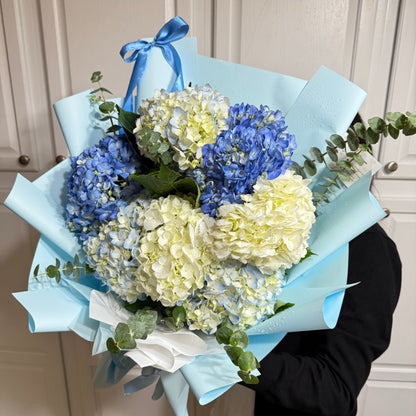 Blue and white hydrangea bouquet wrapped in light blue paper with water droplets.