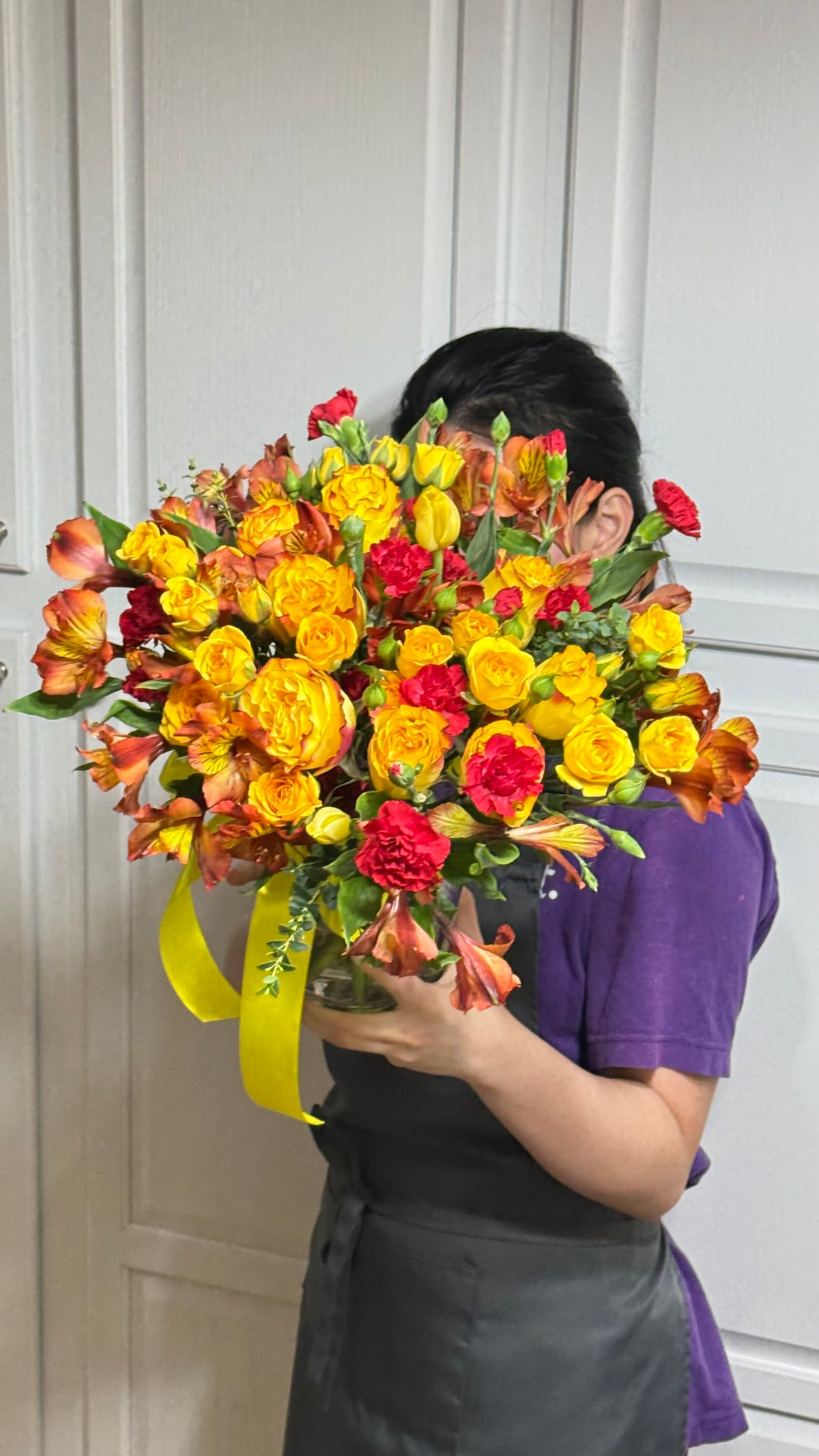 Vibrant yellow, orange, and red flowers in a large bouquet with a yellow ribbon.