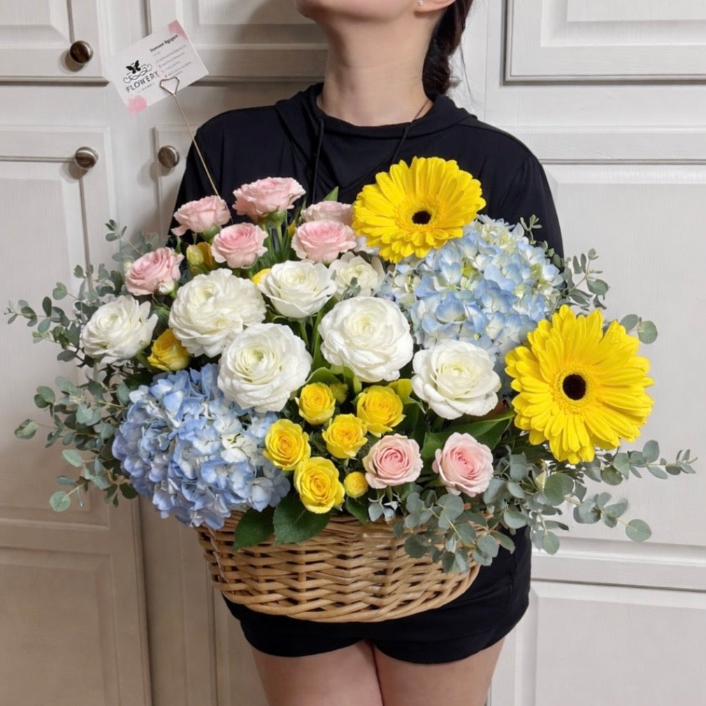 Large wicker basket filled with vibrant white, blue, yellow, and pink flowers.