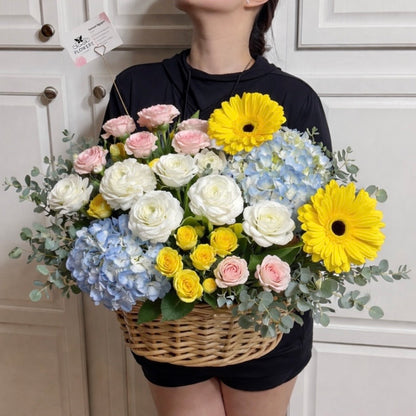 Large wicker basket filled with vibrant white, blue, yellow, and pink flowers.