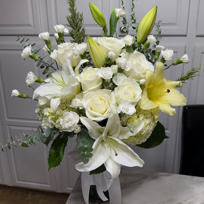 A full white and yellow floral arrangement with roses, lilies, and green leaves.