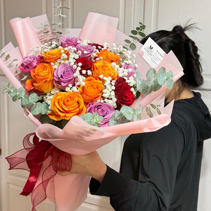 A person holds a vibrant bouquet of orange, purple, and red roses with baby's breath.