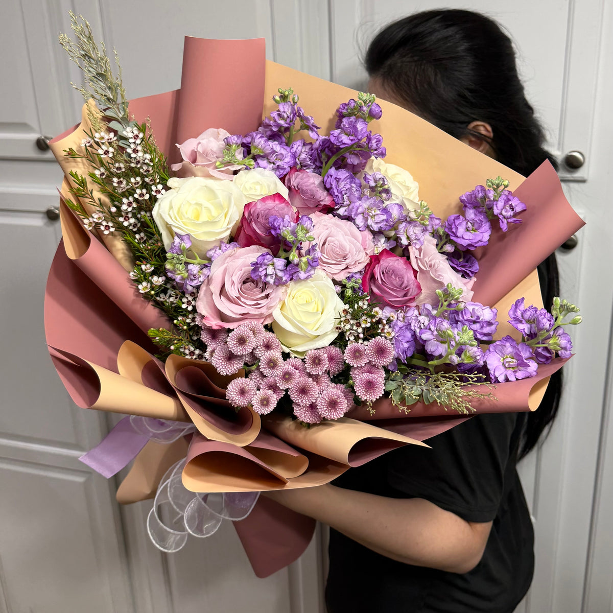Large bouquet of white, pink, and purple flowers wrapped in two-toned paper.