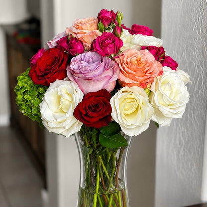 Vibrant bouquet of red, white, pink, and purple roses in a clear vase.