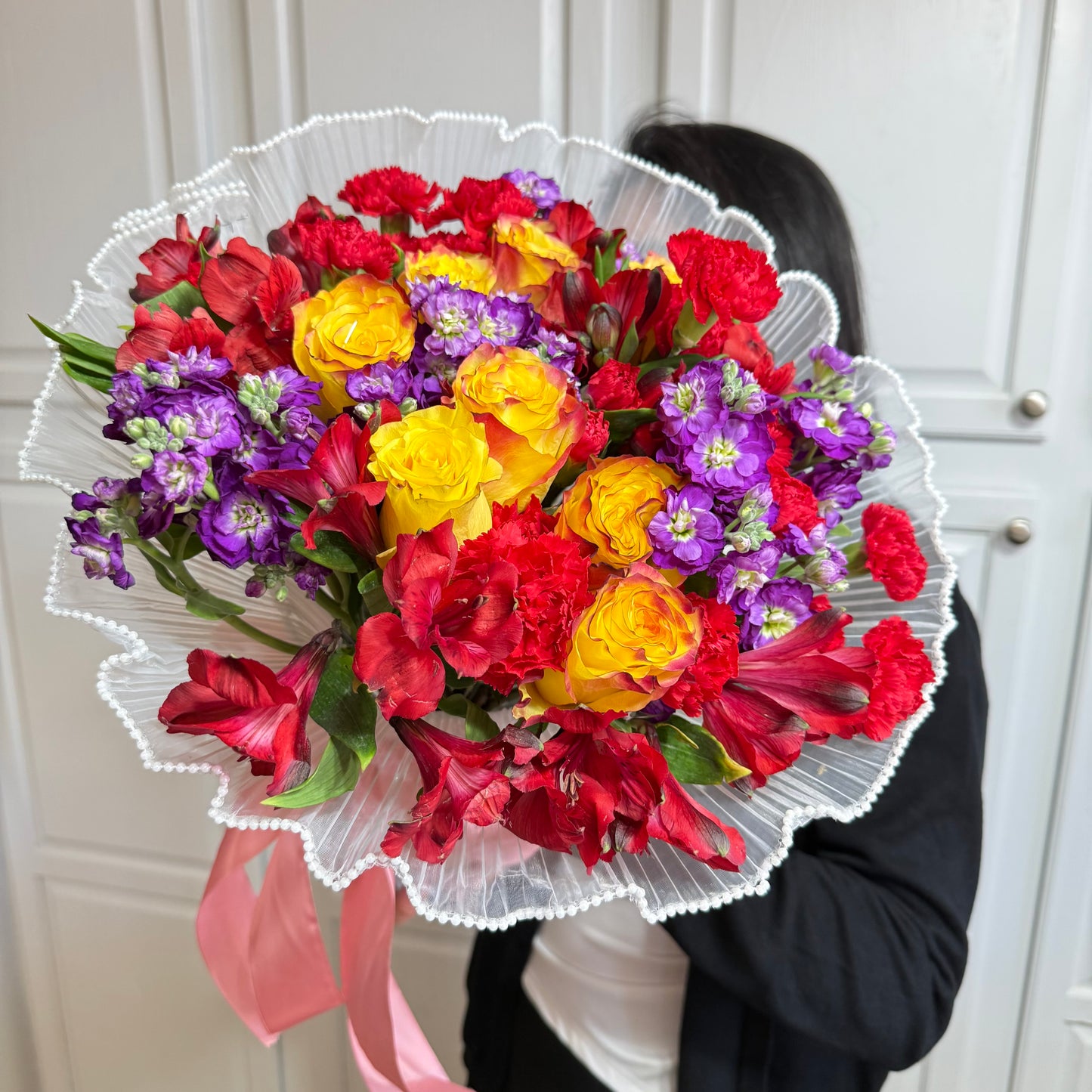 Vibrant bouquet of yellow roses, red carnations, and purple flowers in white ruffled wrap.