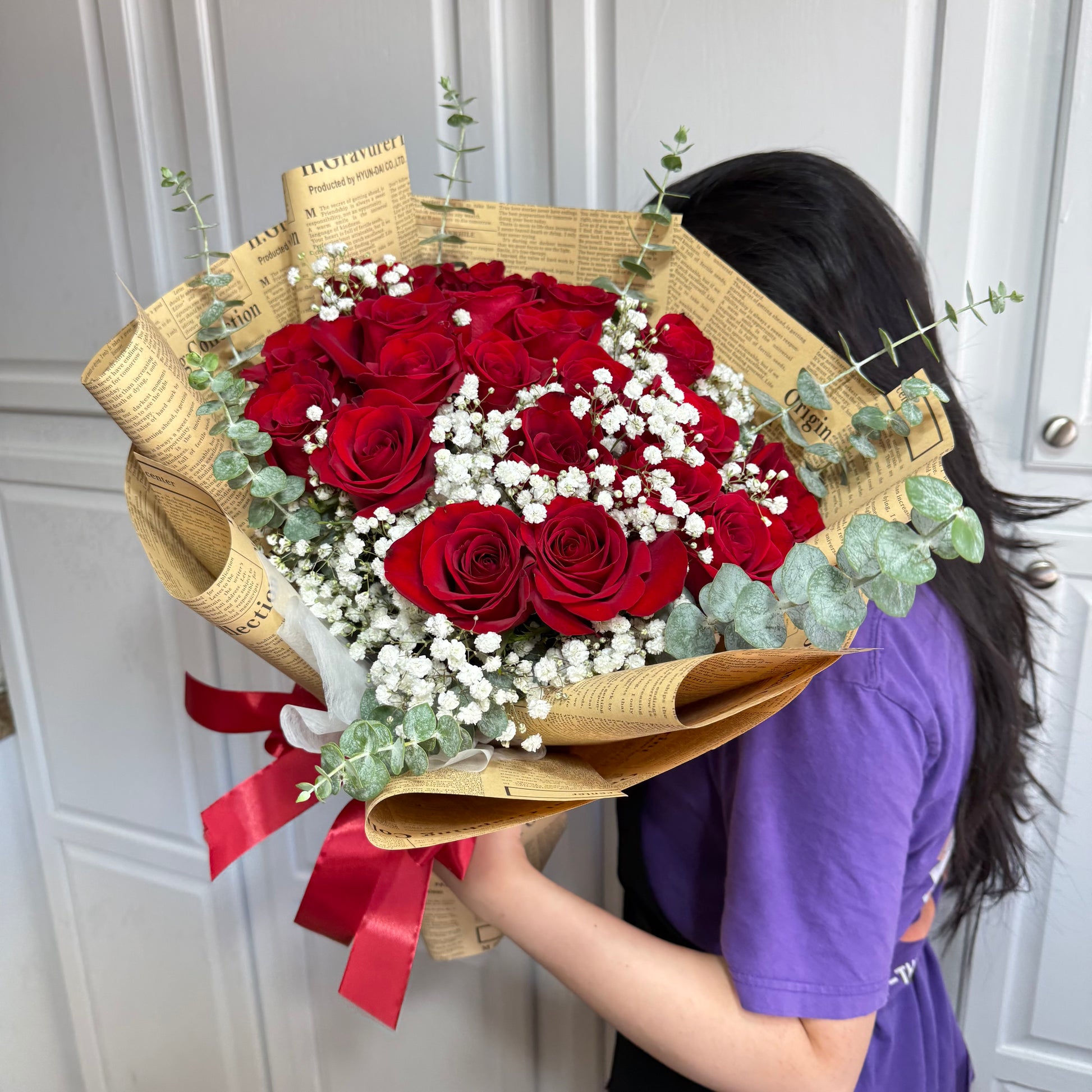 Red roses and white flowers in a vintage paper bouquet with a red ribbon.