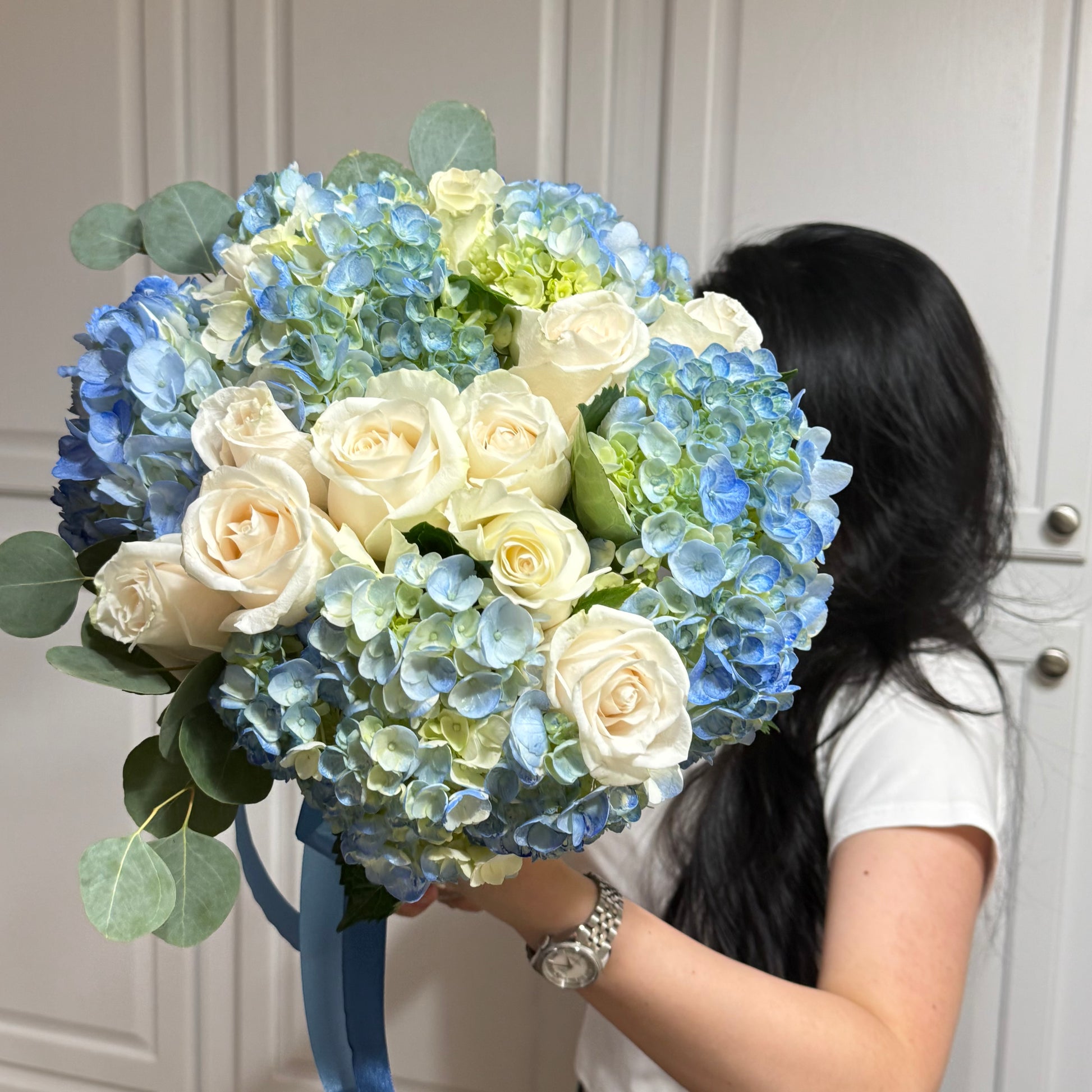 Round bouquet of blue hydrangeas, white roses, and eucalyptus leaves.