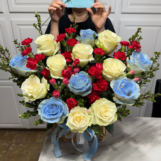 Vibrant bouquet featuring yellow and blue roses, red carnations, and greenery in a basket.