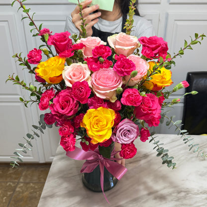 Vibrant bouquet of pink, yellow, and purple roses with fuchsia carnations.