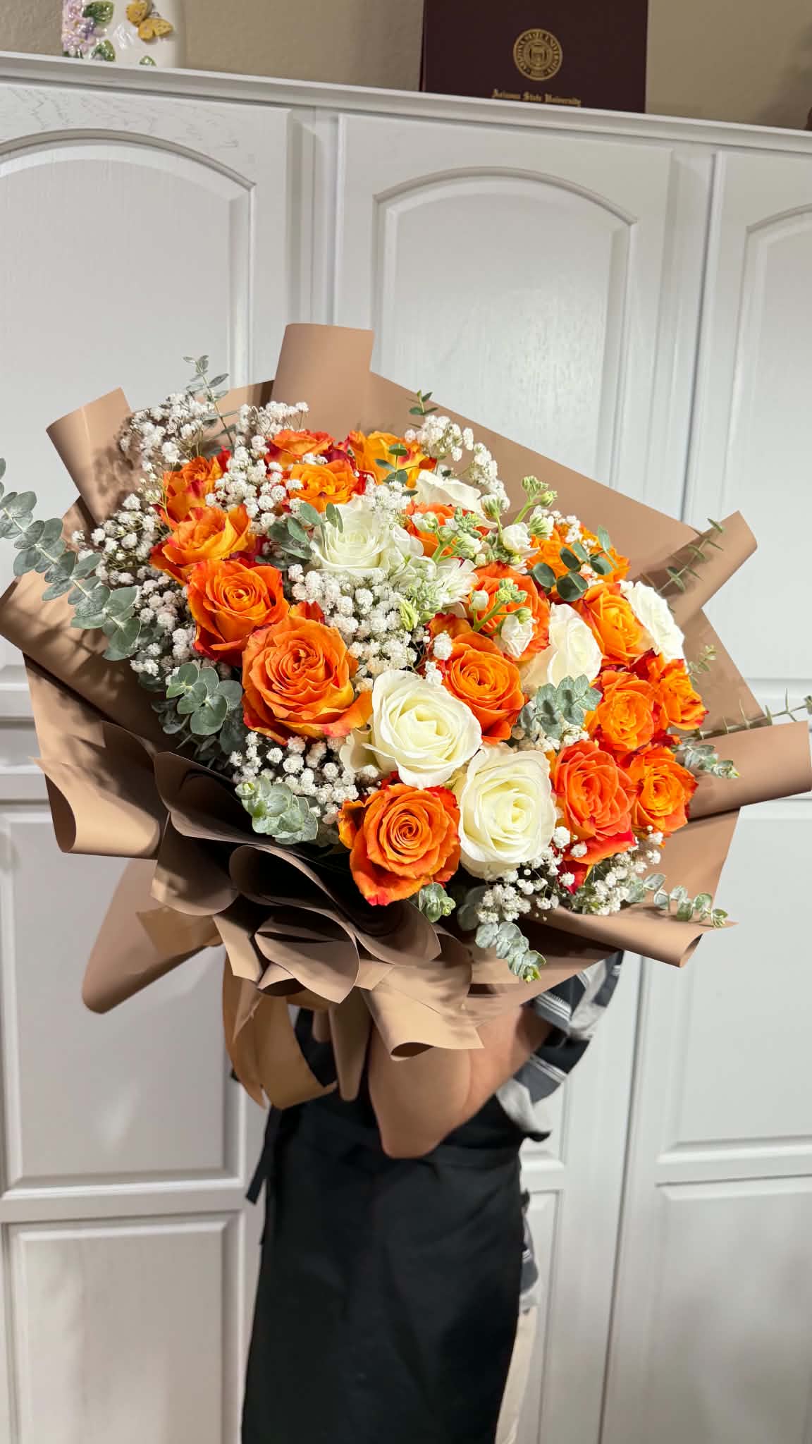 Vibrant orange and white roses in a large, brown-wrapped bouquet.