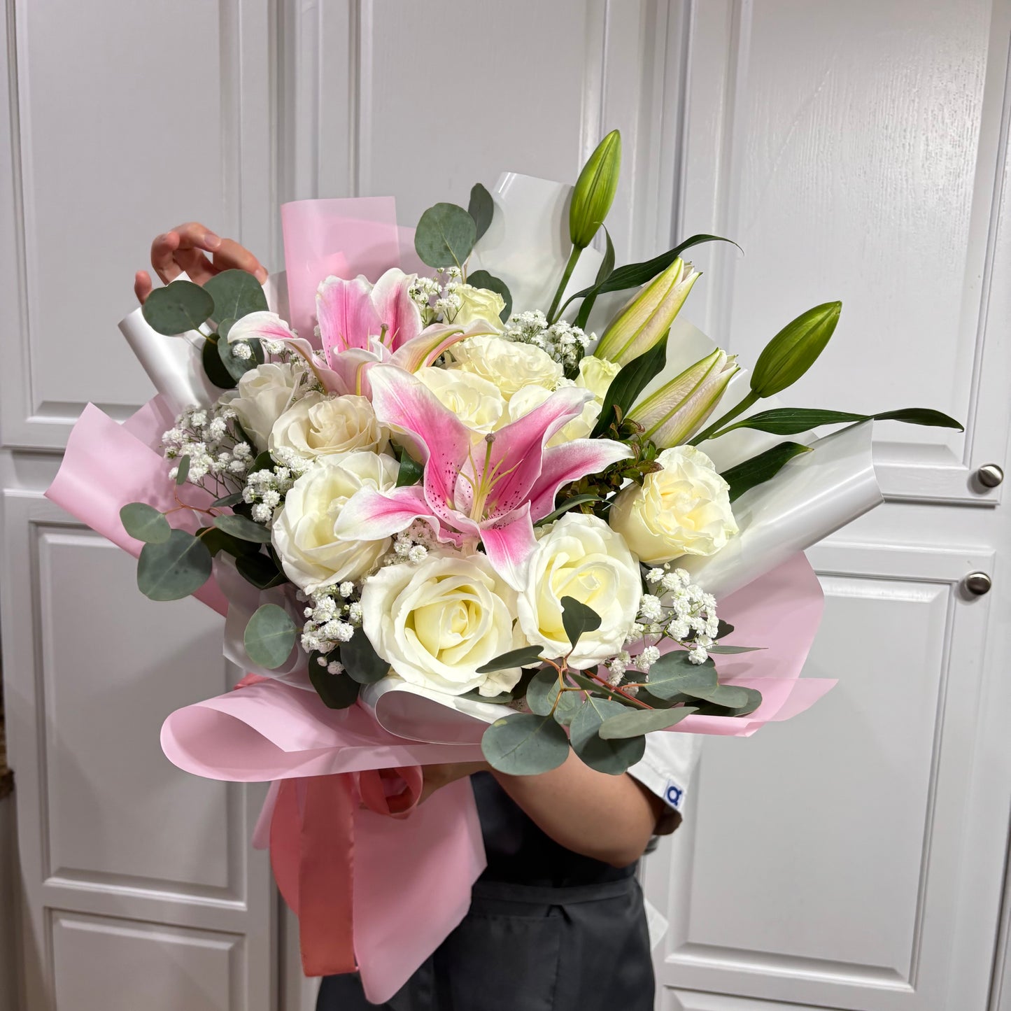Pink and white bouquet with white roses, pink lilies, and green leaves.