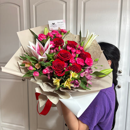 Vibrant bouquet of red roses, pink lilies, and mixed flowers in beige wrap.