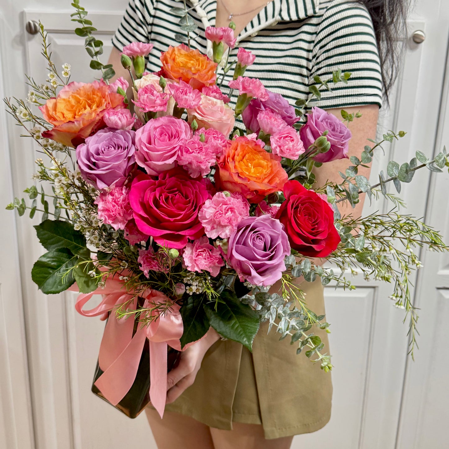 Vibrant bouquet of pink, purple, orange, and red roses with green foliage.