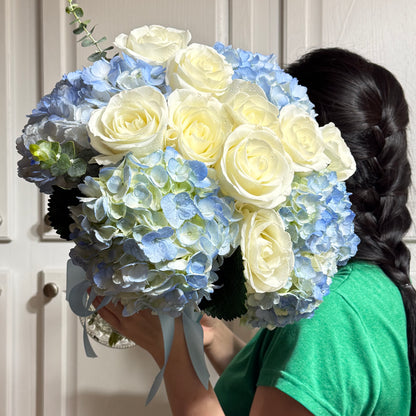 A person holds a large bouquet of white roses and blue hydrangeas.