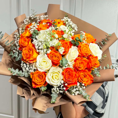Vibrant orange and white rose bouquet with baby's breath wrapped in brown paper.