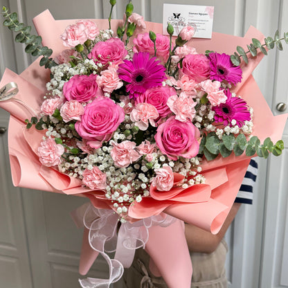 A vibrant bouquet of pink and fuchsia roses, carnations, and gerberas wrapped in pink paper.