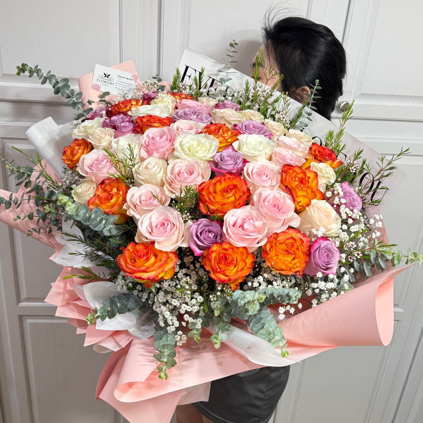 Vibrant bouquet of pink, orange, white, and purple roses wrapped in pink paper.