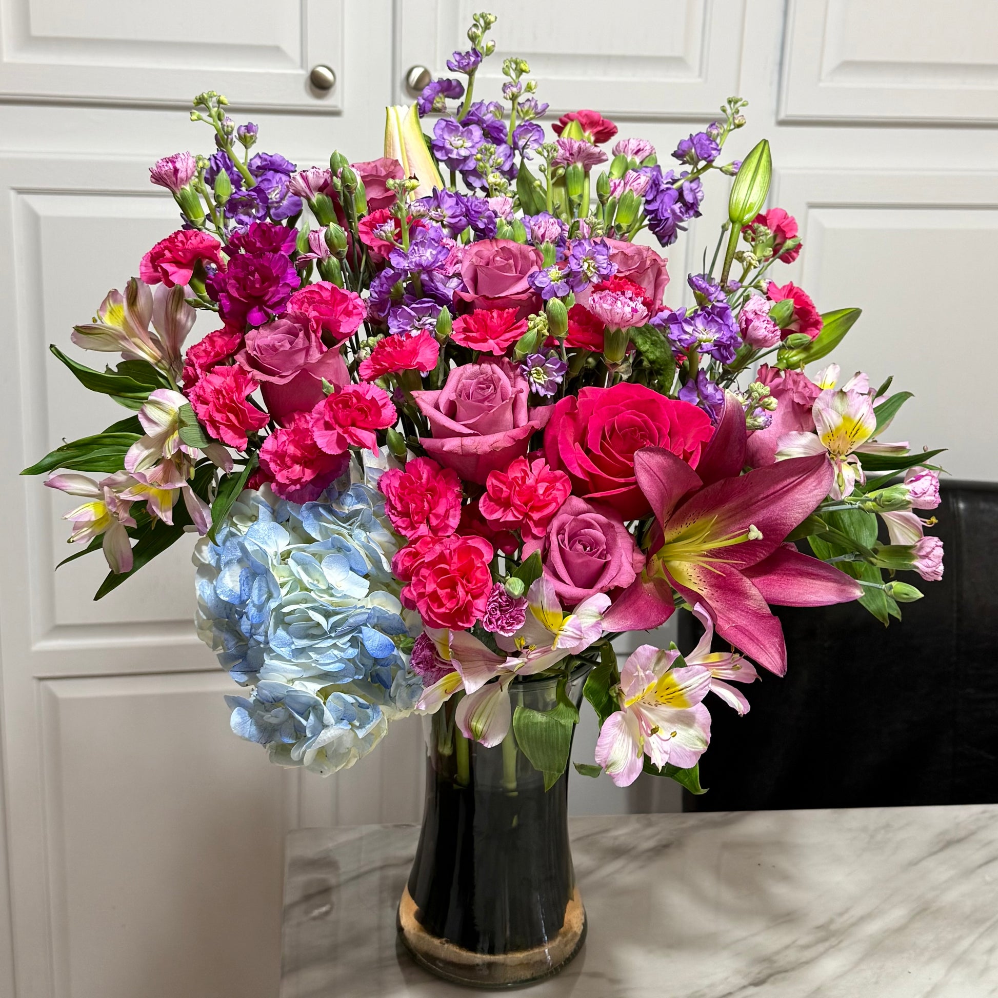 A vibrant bouquet of pink, purple, and blue flowers in a clear glass vase.
