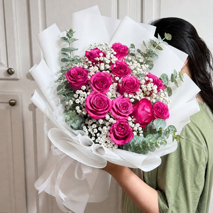 A person holds a bouquet of vibrant pink roses, white baby's breath, and eucalyptus.