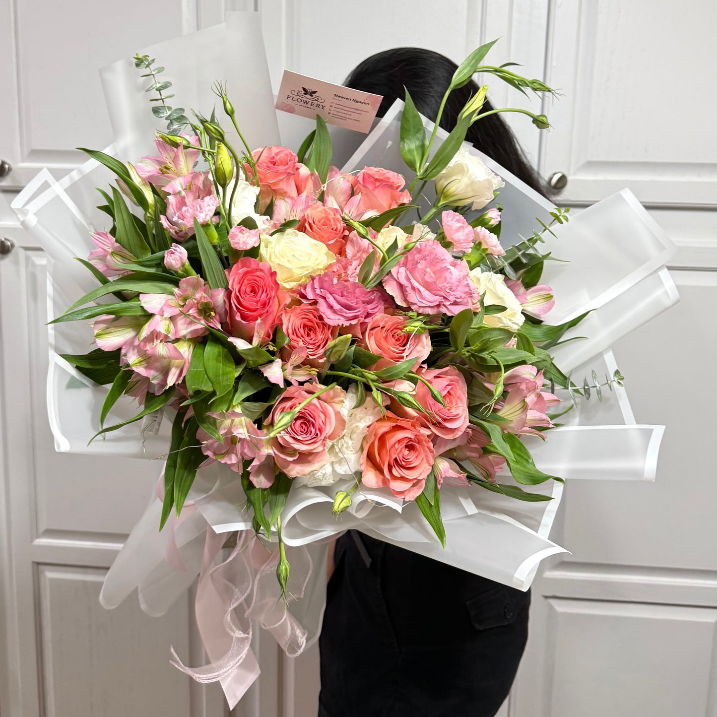 Large bouquet of pink, coral, and white flowers wrapped in white paper.