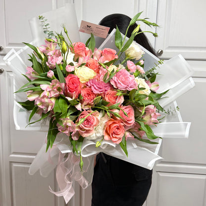 Large bouquet of pink, coral, and white flowers wrapped in white paper.