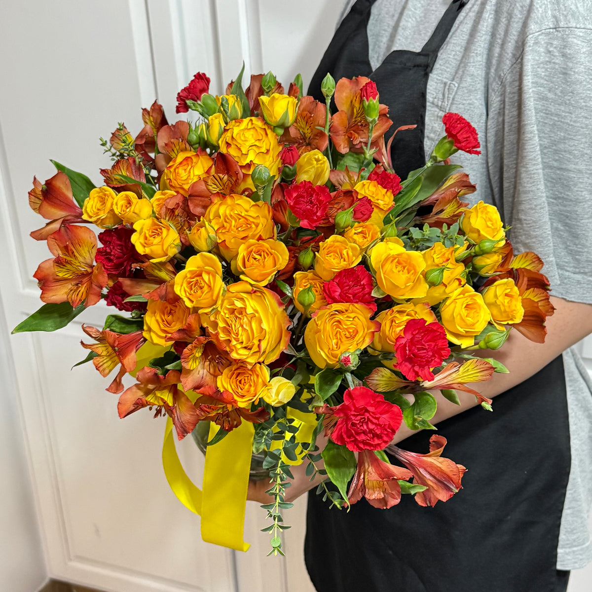 A vibrant bouquet of yellow roses, orange alstroemeria, and red carnations.