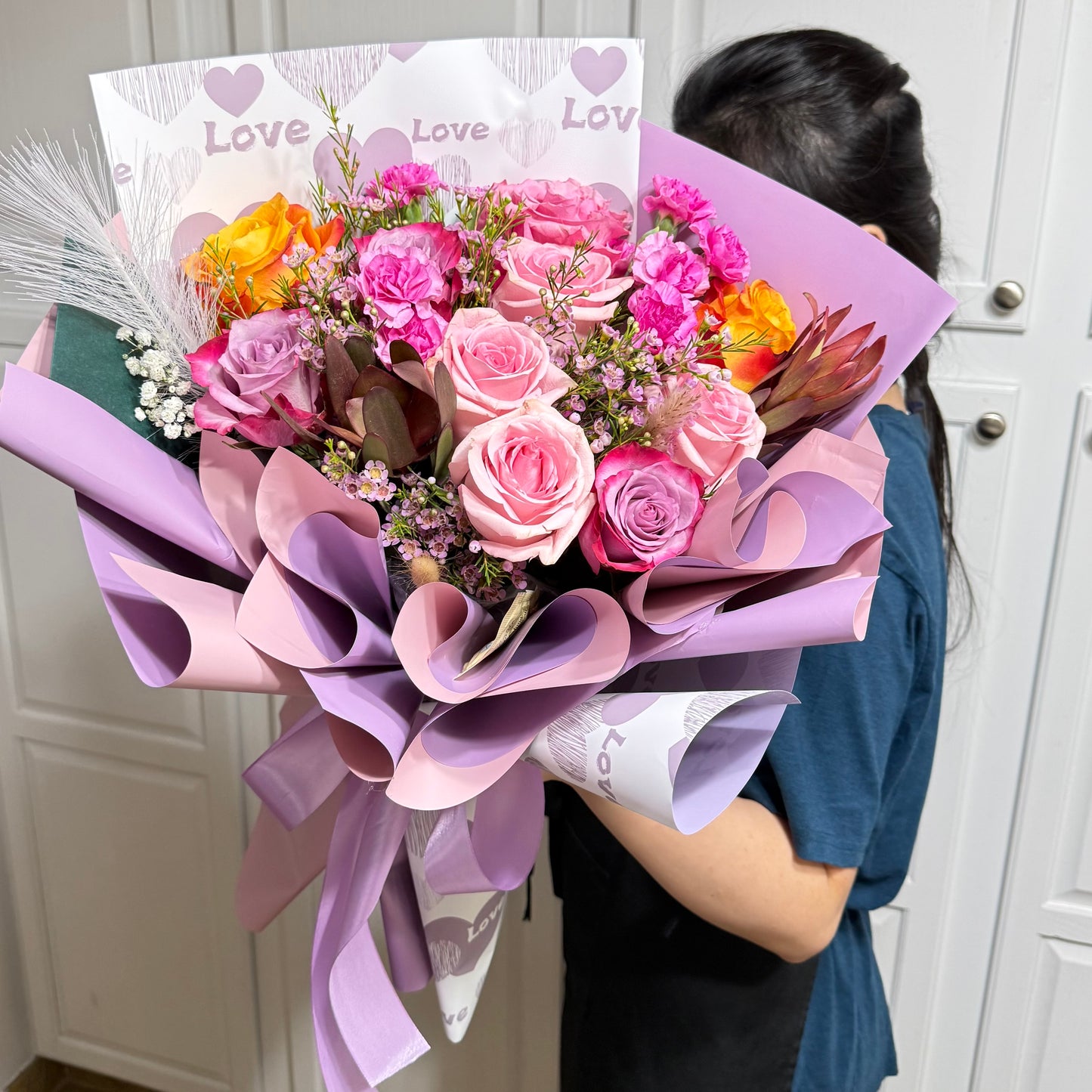 A vibrant bouquet of pink, purple, and orange roses wrapped in purple paper.